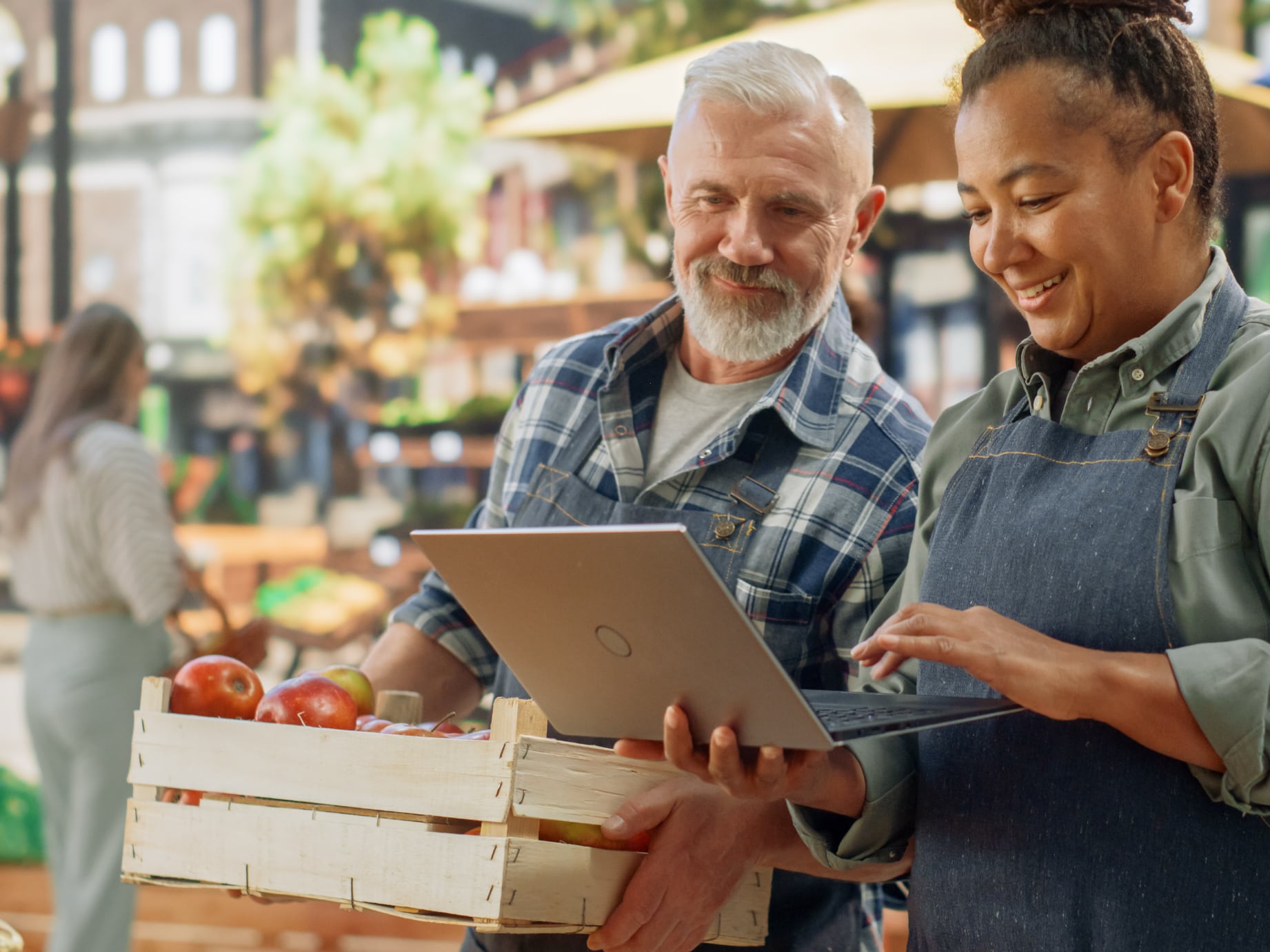 Older white man and adult, black woman looking at a laptop with an urban farm stand behind them